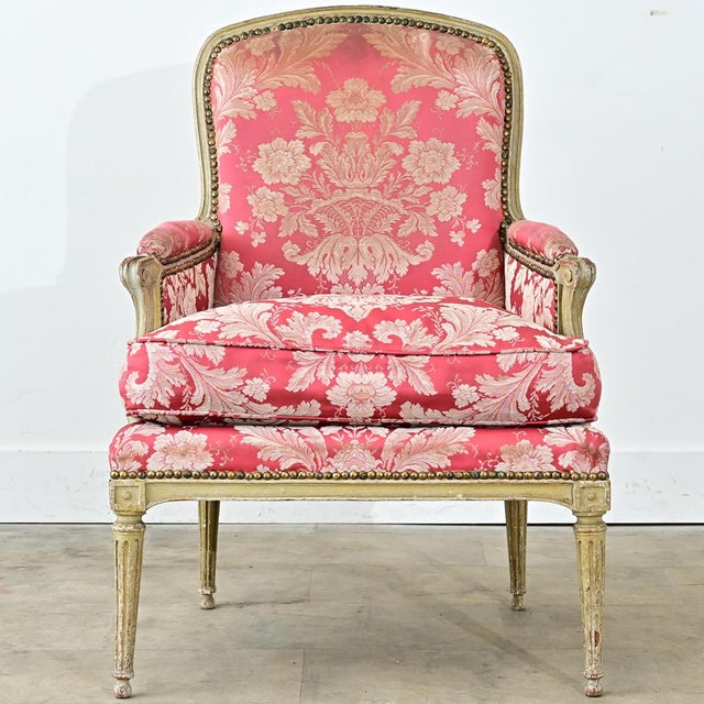 A French Louis XV – Louis XVI transitional bergere with carved details and a painted finish. The chair has a curved back...