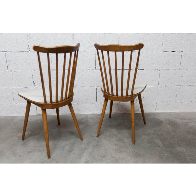 Discover this pair of Baumann Menuet chairs, a true ode to vintage design. with their honey-patina finish and white vinyl...
