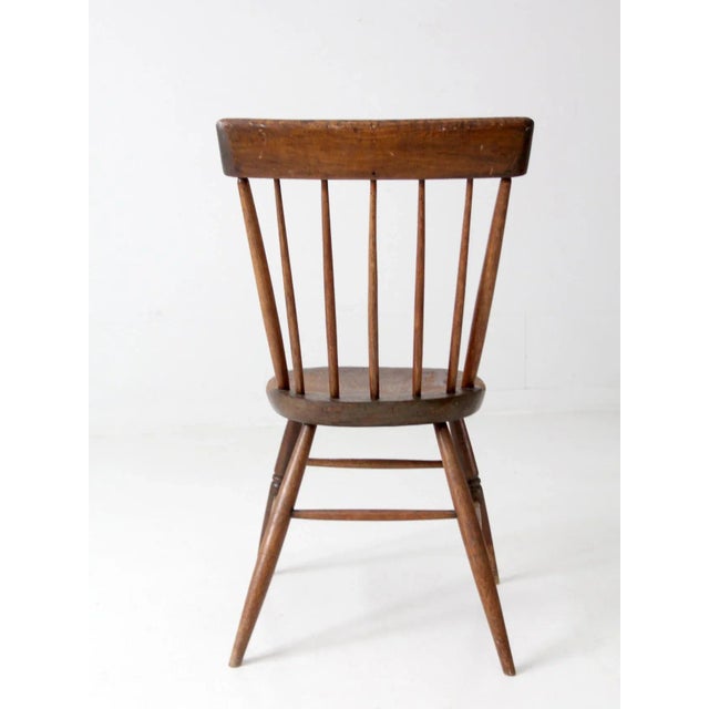 This is an antique farmhouse chair. The primitive dining or side chair features a plank seat, spindle back, and turned legs.