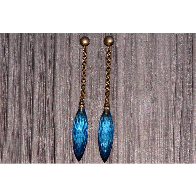 The Bourges: Blue Topaz Briolette Dangler Statement Earrings in Yellow Gold. The earrings feature elongated Swiss blue...