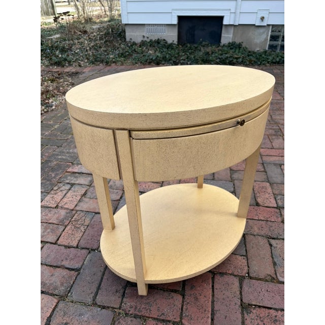 Oval side or bedside table with a pull-out shelf, drawer and base shelf. Designed by Charles Pfister for Baker Furniture....