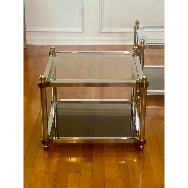 Handsome pair of 1970's two tier brass and polished steel square tables in the manner of Maison Jansen. The lower tier...