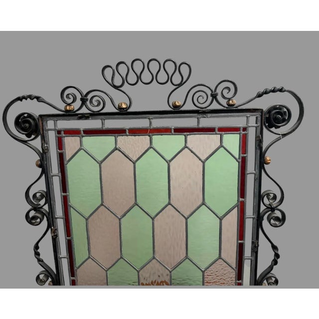 An antique Arts and Crafts fire screen offers wrought iron frame construction with stylized scroll elements and added...