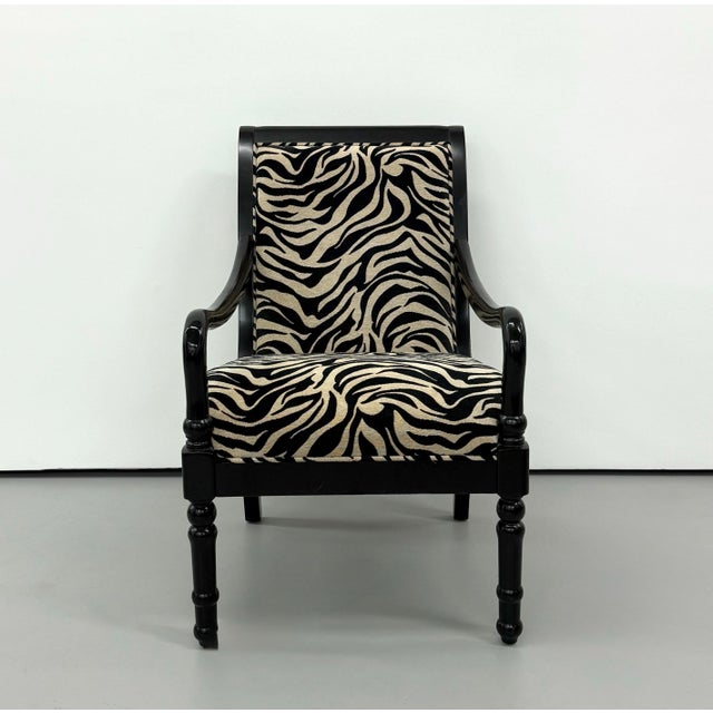 A dramatic vintage armchair featuring a glossy ebonized wood frame with gracefully curved arms, turned front legs, and a...