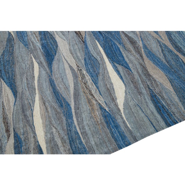 Beautiful modern flat-weave Kilim handmade wool rug featuring a blue field. This Kilim rug showcases earthy tones in a...