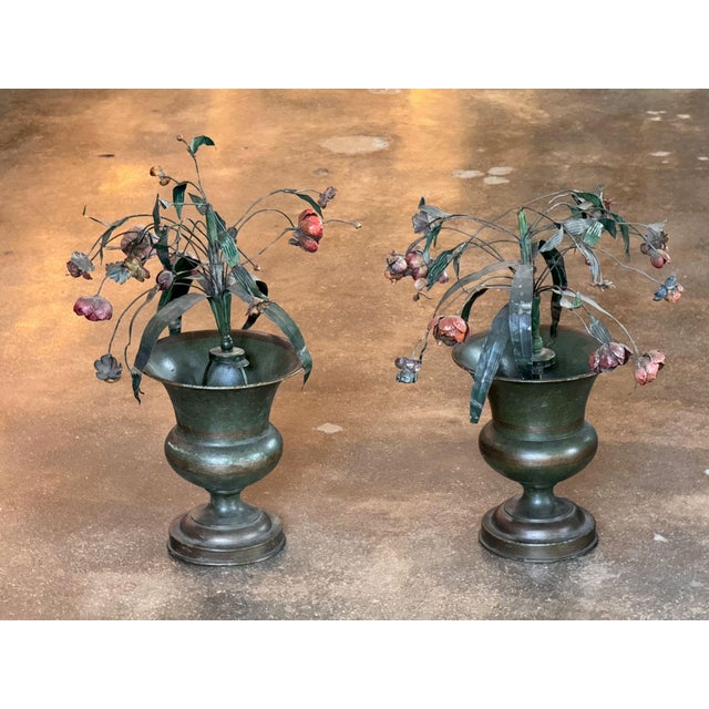A pair of tole urns of classical campana form on stepped socle bases, each filled with a spray of painted tole flowers,...