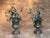 A pair of tole urns of classical campana form on stepped socle bases, each filled with a spray of painted tole flowers,...