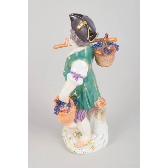 Meissen, grape boy figurine. Porcelain figurine depicting a boy carrying baskets filled with grapes, finely hand-painted...