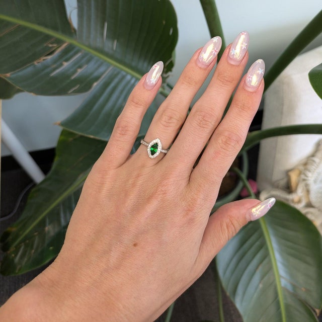A natural tsavorite garnet from Tanzania glows green in a marquise silhouette, framed by diamonds in this estate-style...