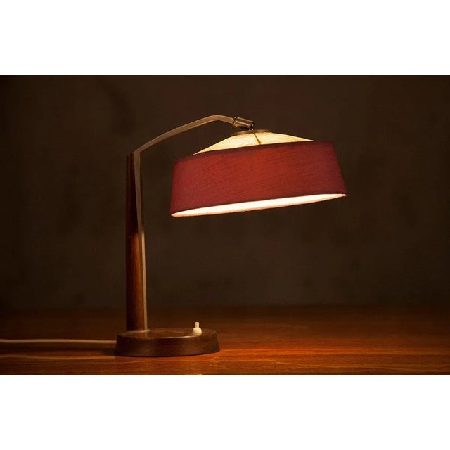 Danish table lamp featuring a solid teak base from which metal is protruding, and a fabric shade in beige and pink....