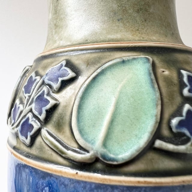 A striking antique stoneware vase from the Royal Doulton Lambeth studio. The design features a tube-lined collar foliage...