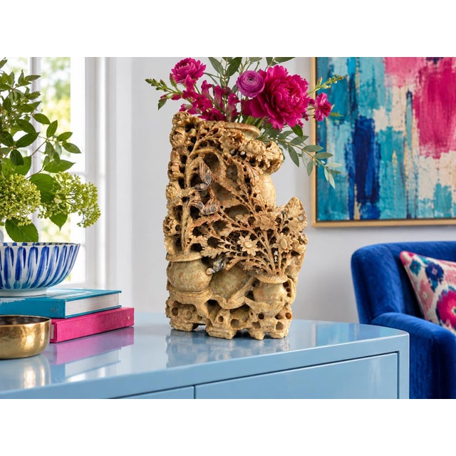 An intricately carved stone vase featuring birds nestled among flowering branches, layered foliage, and sculptural vessel...
