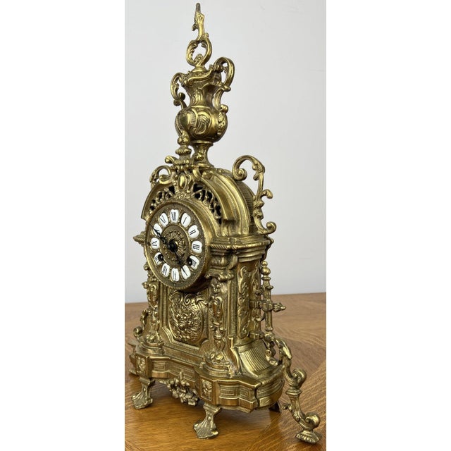 A striking Vintage French brass clock with an exceptionally ornate design, featuring intricate scrollwork, decorative cast...