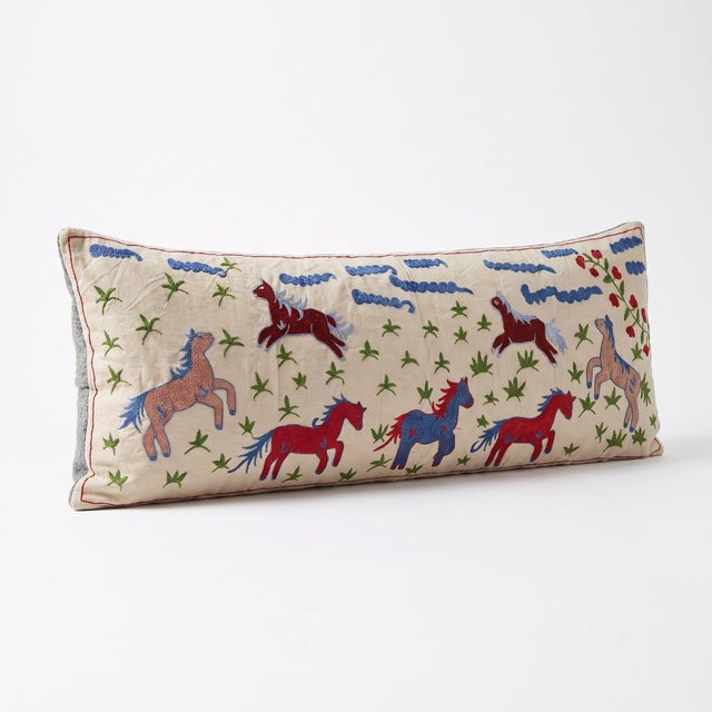 An extra-long lumbar pillow cover made from hand-embroidered Uzbek Suzani cotton — red and blue galloping horses on cream...