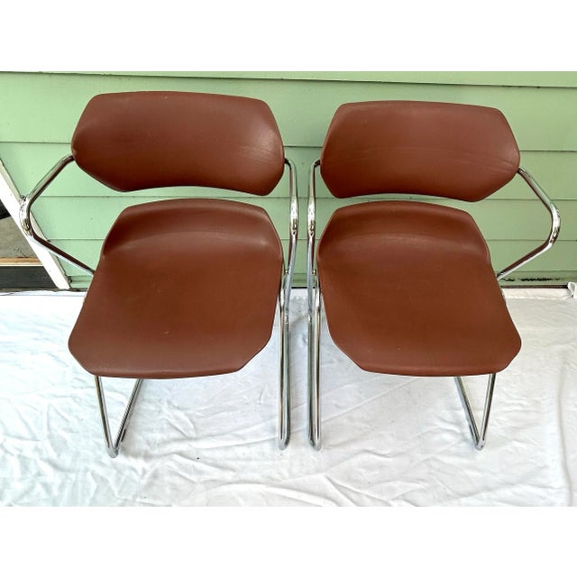 Pair of vintage 1970s stacking chairs with molded brown vinyl seats and polished chrome frames. Their compact, sculptural...