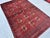 This hand-knotted Mauri Bokhara rug features bold, finely woven octagonal guls set in a neat grid across a deep madder-red...