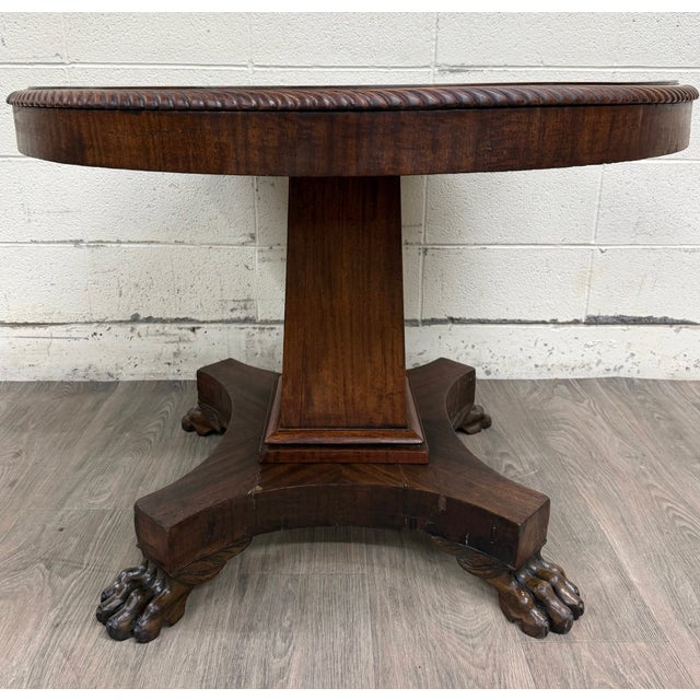 This is a striking antique American Empire mahogany pedestal round center table with carved paw feet or lion feet, likely...