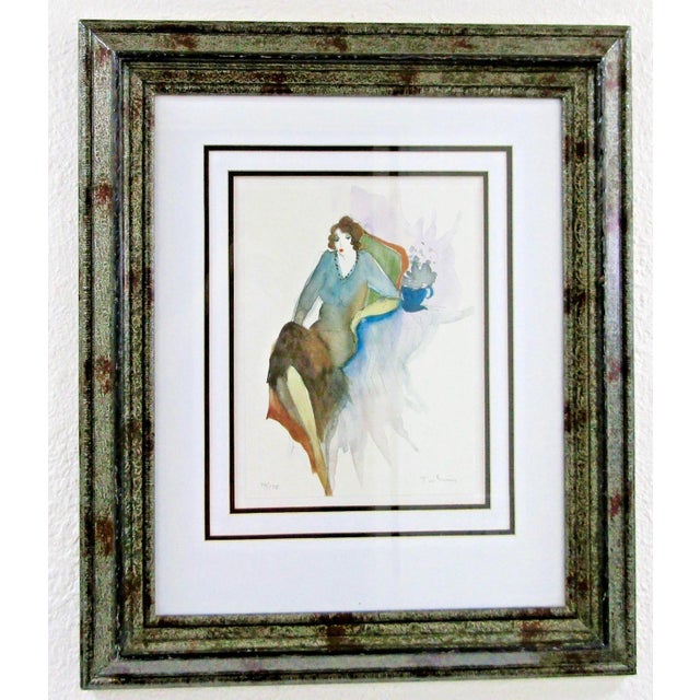 This is a signed and numbered lithograph by artist Itzchak Tarkay depicting a seated woman with a coffee. This medium-...