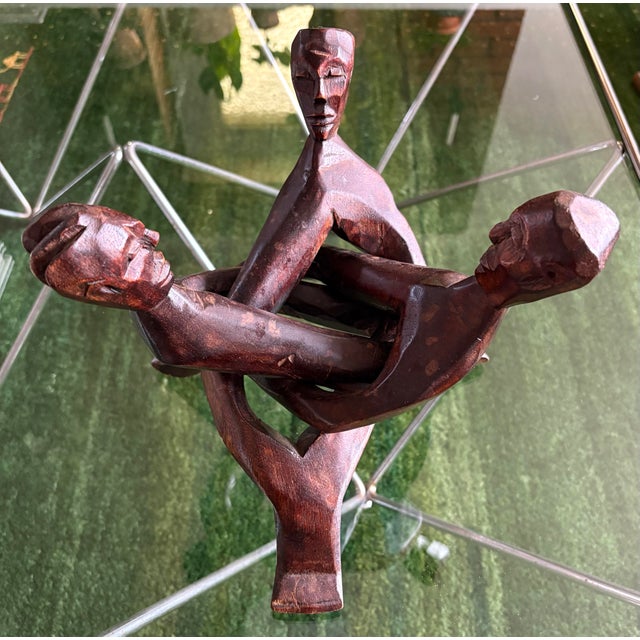 Striking vintage hand-carved wood sculpture featuring three stylized human figures intertwined in an intricate, almost...