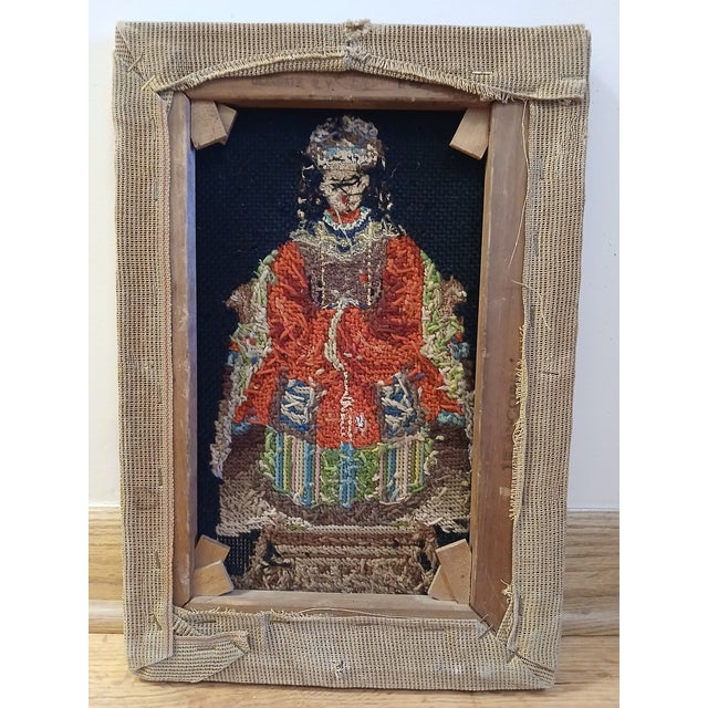 This piece displays deep black fabric surrounding a figure rendered in warm red, cream, and muted green threads, with the...