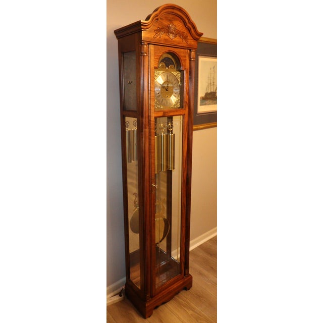 A finely crafted floor clock by Howard Miller, presented in a warm Windsor Cherry finish with traditional bonnet pediment...