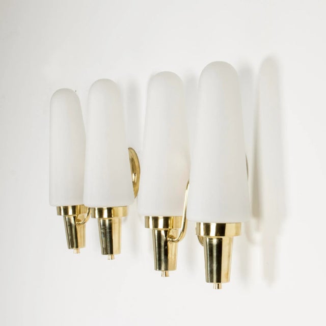 This pair of brass wall lamps features double opaline glass shades shaped like sugarloafs. European Plug (up to 250V).The...