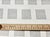 Designer fabric with a pattern of gray striped rectangles on an off white background. The rectangles are arranged in a...