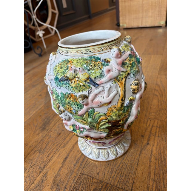 A striking 18-inch Italian Capodimonte porcelain covered urn, richly decorated with exuberant figural cherubs in full...