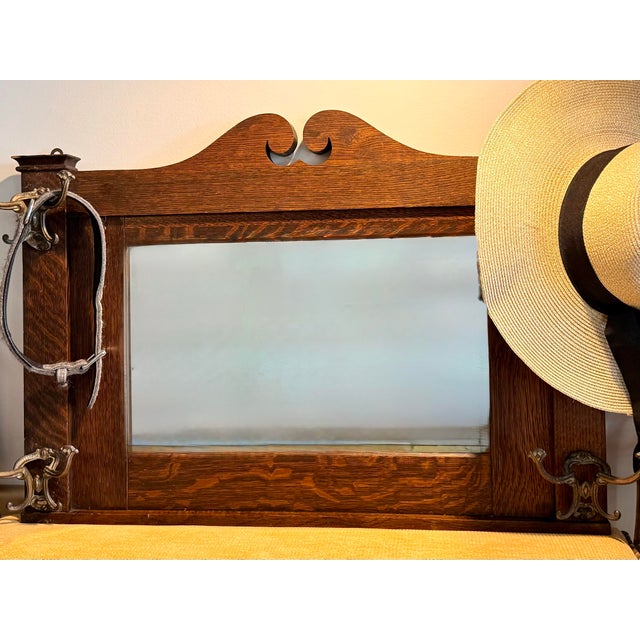 A handsome antique hall mirror crafted in richly figured tiger oak, with a broad beveled mirror and four ornate cast-metal...