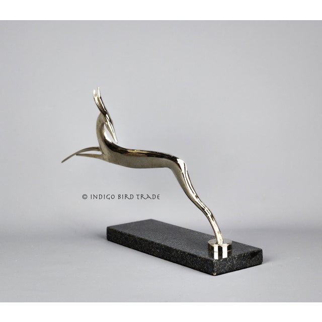 An elegant Art Deco sculpture features a chromed metal leaping gazelle mounted on a black marble base. It is made in a...