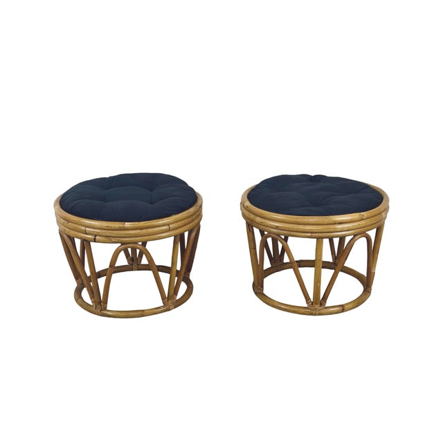 A charming pair of vintage rattan and bamboo-style footstools featuring sculptural openwork frames, warm honey-colored...