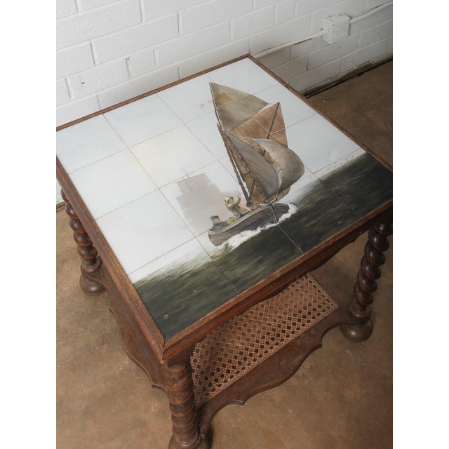 This charming antique oak side table features a unique hand-painted tile top depicting a nautical sailing scene—a...