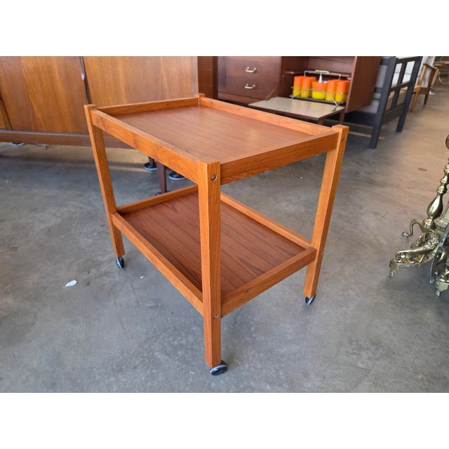 Bring timeless Scandinavian warmth and functionality into your home with this handsome Mid-Century Modern teak rolling bar...