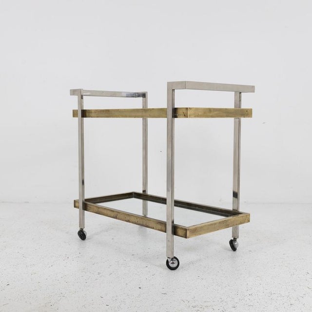 Two-shelf bar cart featuring a square-section chrome-plated iron frame and brass shelf frames. The two shelves are topped...