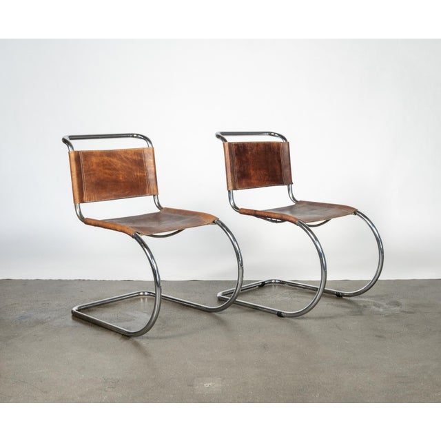 Elegant pair of Bauhaus-inspired cantilever chairs featuring tubular chrome-plated steel frames and brown leather sling...