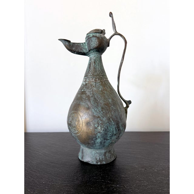 A large cast bronze ewer with hinged lid and stylized scroll handle dated 11-12th century from Seljuk Period. The medieval...