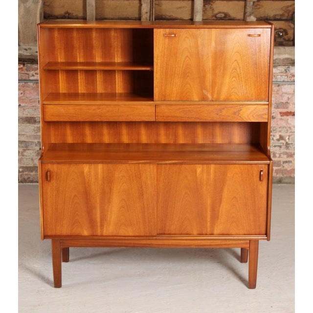 A midcentury teak drinks cabinet/highboard made in teak with a cupboard to the base, open shelving above, two drawers and...