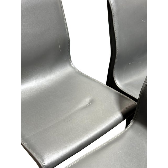 Set of 6 dining chairs with a modern design. Milky gray leather, visible stitching, fastened onto a simple steel frame....