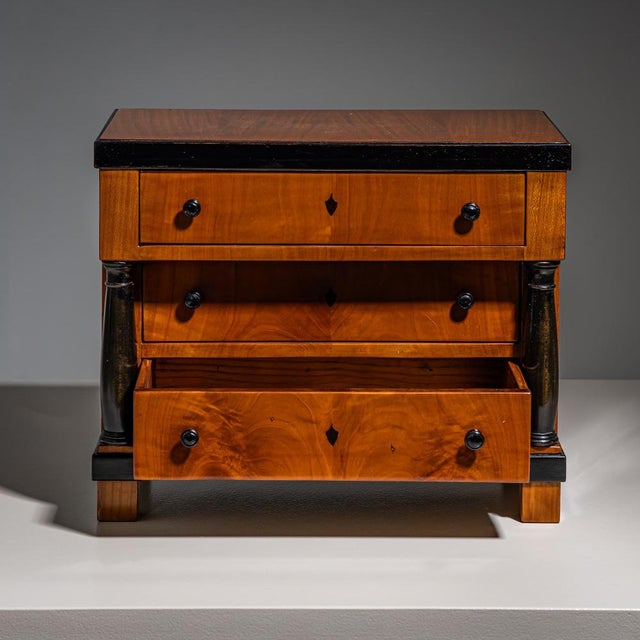 Biedermeier miniature chest of drawers in cherrywood with ebonised columns and decorative details. The three-drawer piece...