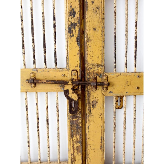 This pair of antique wood and iron doors features primitive yellow-painted wood with white iron barred windows. Each door...