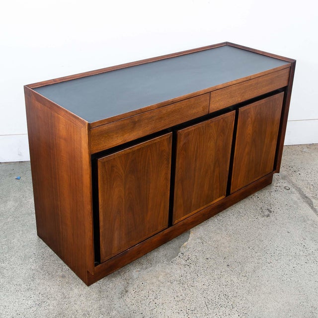 Compact walnut credenza with a black laminate top by Dillingham. This piece includes 3 drawers and 3 doors. A clean and...