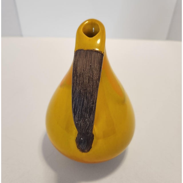 Add a vibrant pop of authentic mid-century warmth to your shelving with this vintage 1970s ceramic handled pitcher vase....