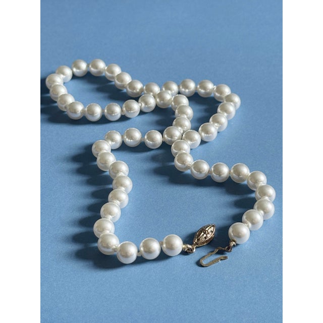 Vintage Mid Century single strand faux pearl necklace featuring bright white pearlized beads and an ornate silvertone...