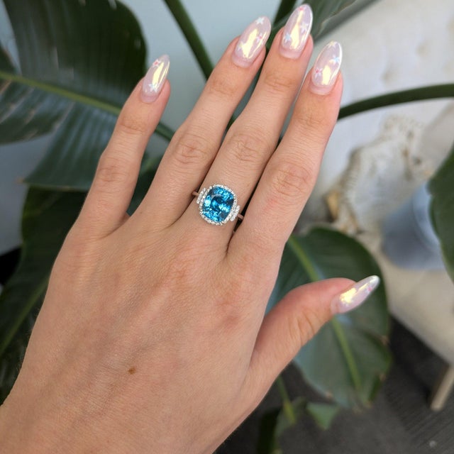 A large Cambodian blue zircon glows electric blue at the center of this cushion ring, wrapped in a brilliant halo of...