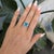 A large Cambodian blue zircon glows electric blue at the center of this cushion ring, wrapped in a brilliant halo of...