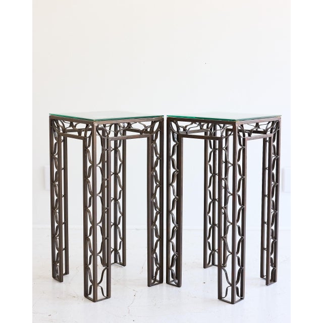 A striking pair of pedestal tables in dark patinated metal, each supporting a square clear glass top. The frames are...