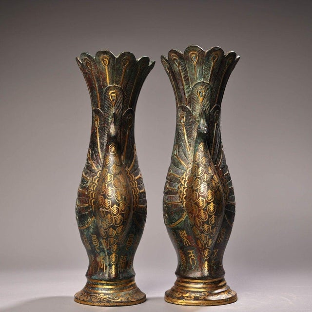 A striking matching pair of archaic-style bronze vases adorned with finely inlaid gold wire forming elaborate peacock...