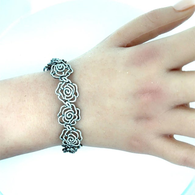 A contemporary link bracelet showcasing intricate rose motifs adorned with round-cut white diamonds. The delicate floral...