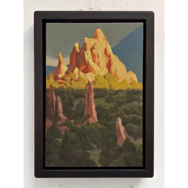 The artwork depicts a rugged mountain landscape bathed in warm, golden light, highlighting the dramatic peaks and rocky...