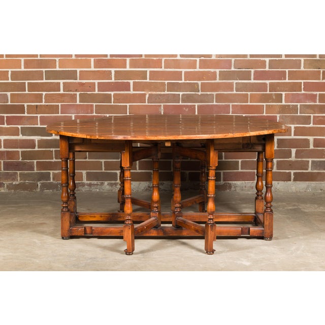 A rustic English pine drop-leaf table from the 19th century with oval top, turned swivel legs, two lateral dovetail...